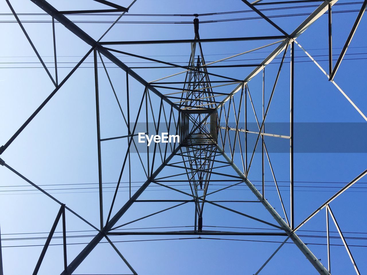 Low angle view of electricity pylon against clear blue sky