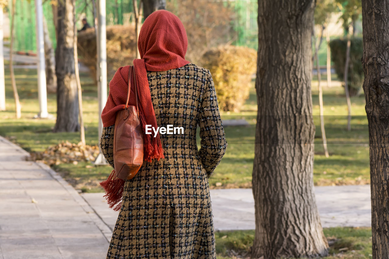 Rear view of woman standing by tree trunk