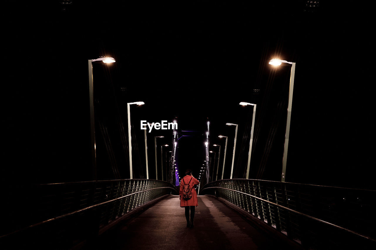 Rear view of woman standing on illuminated bridge at night