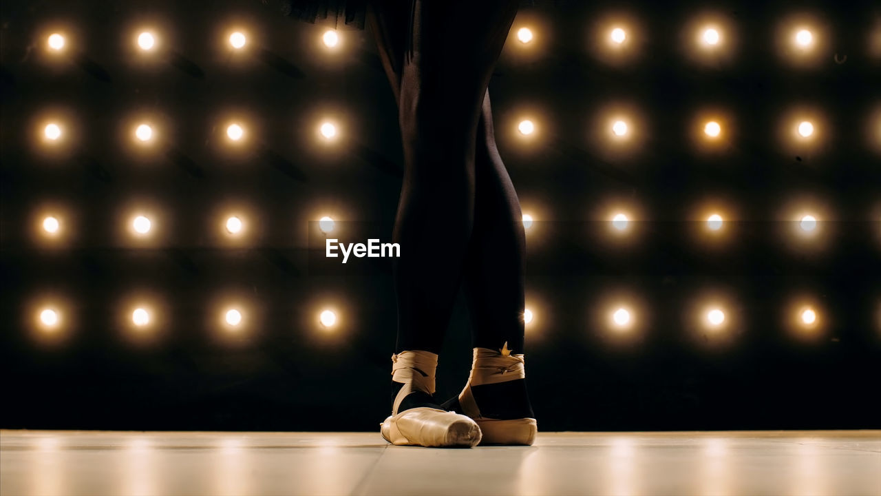 Low section of female ballet dancer standing on stage floor against illuminated lights
