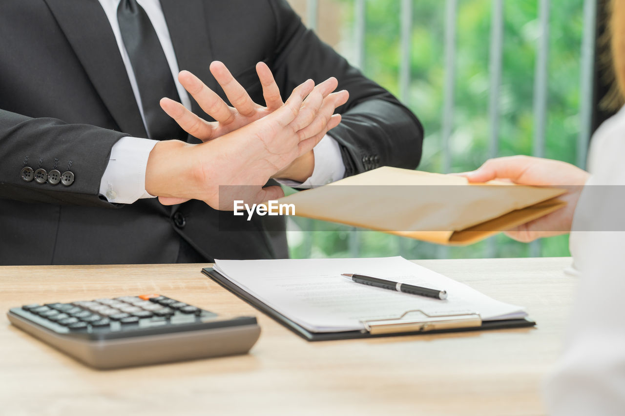 Midsection of businessman showing stop gesture to client giving package on table