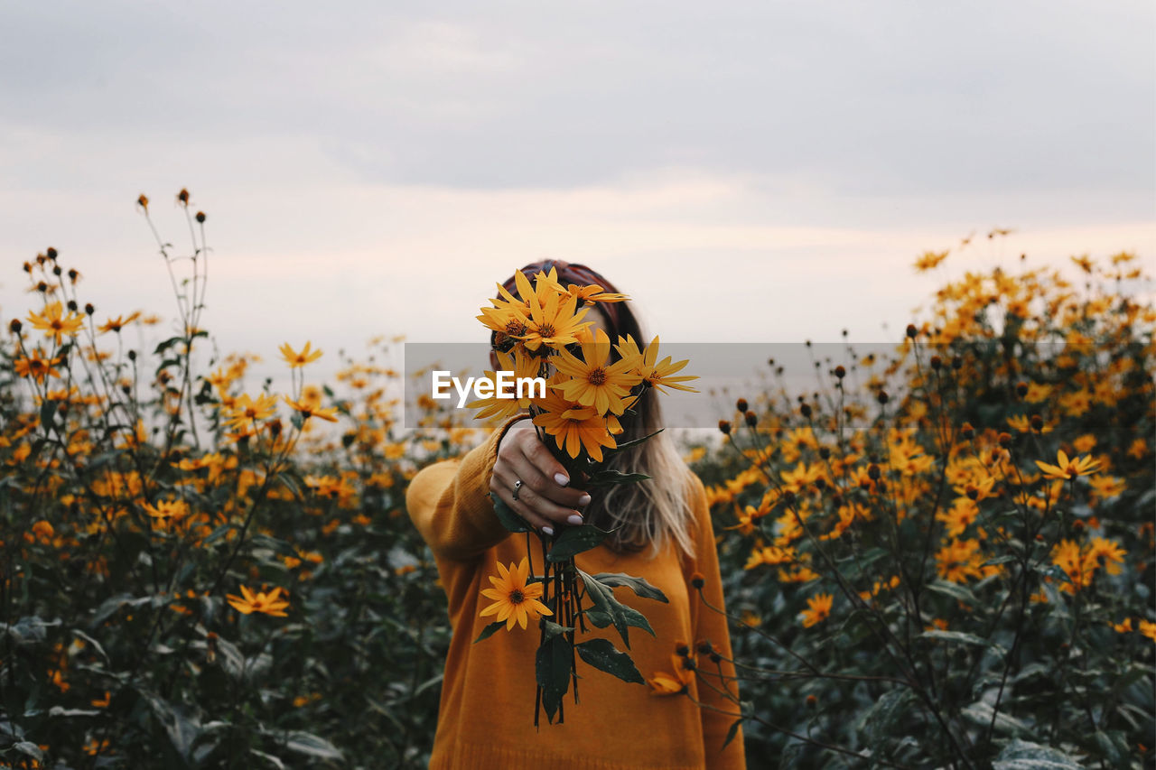 Woman standing on yellow flowering plants on field