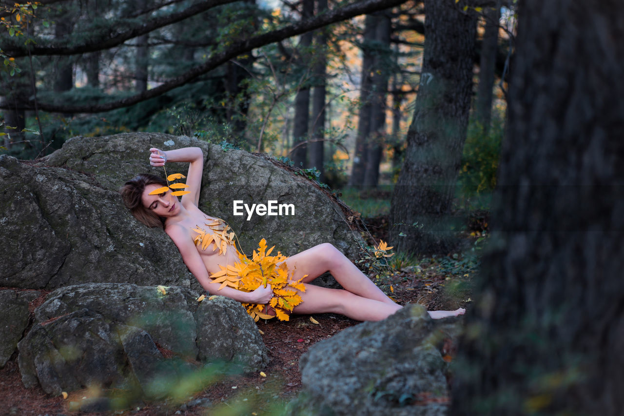 Naked female model lying with leaves in forest