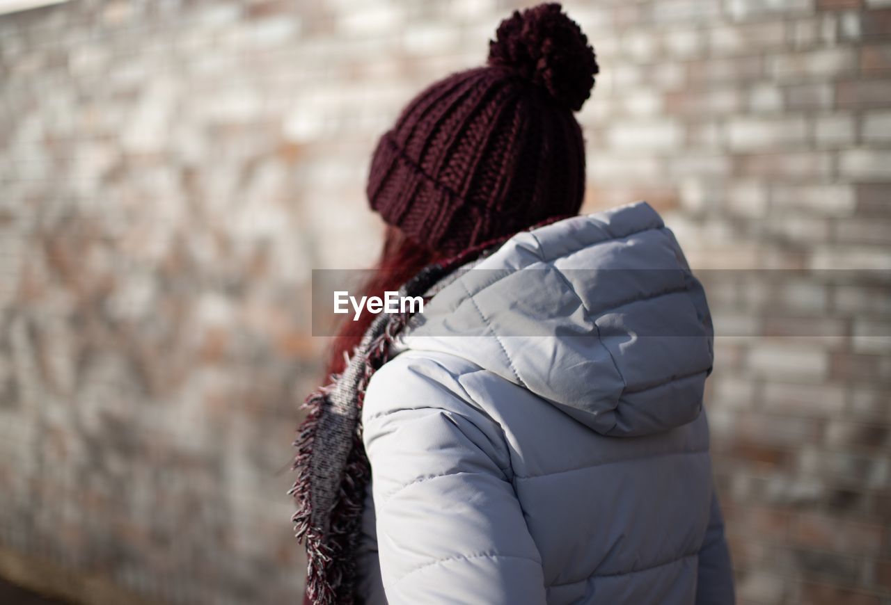 Close-up of woman wearing warm clothing while standing against brick wall