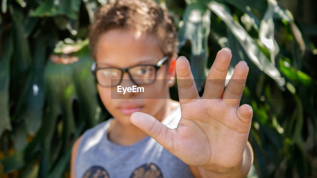 Portrait of boy wearing eyeglasses while gesturing against plants
