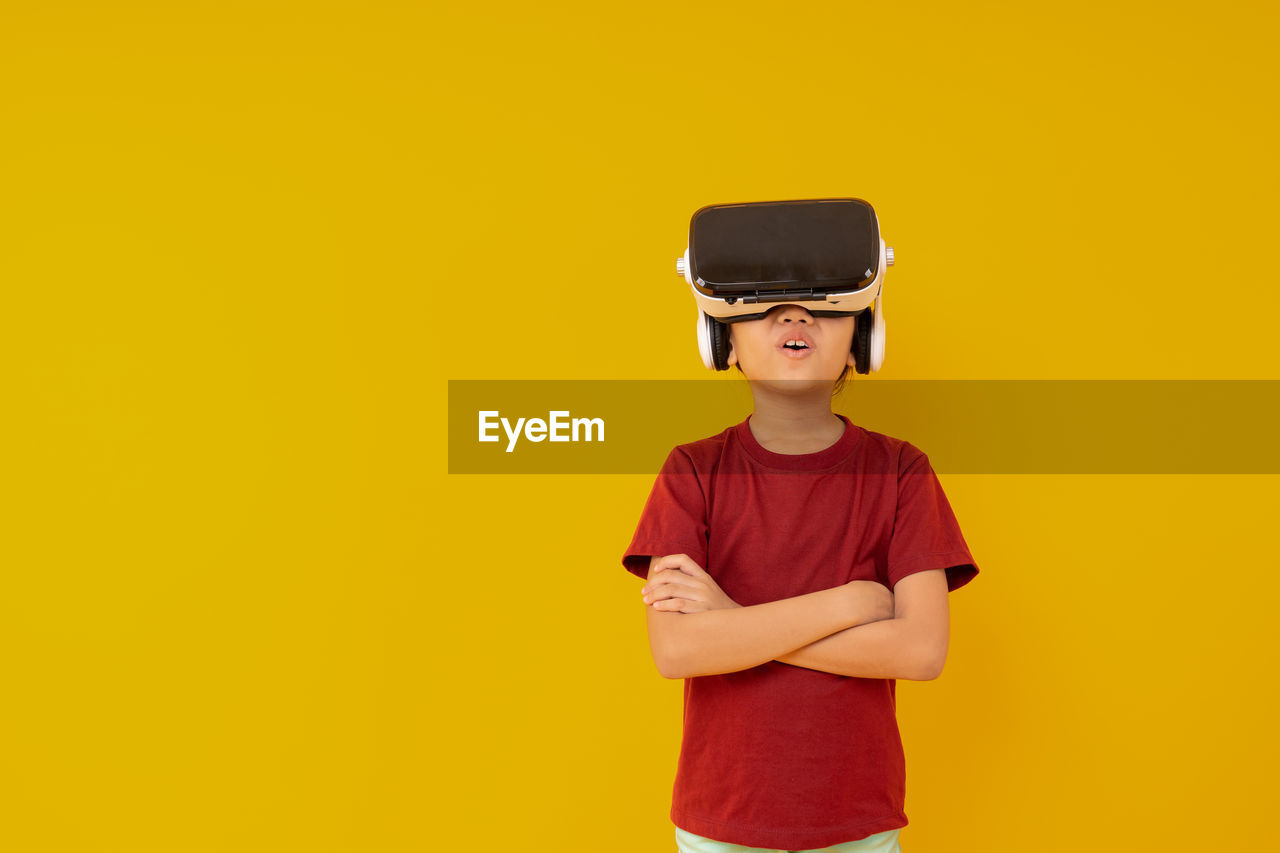 Boy wearing vr box standing against yellow background