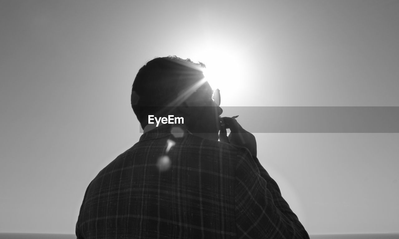 Rear view of man smoking cigarette against clear sky during sunny day