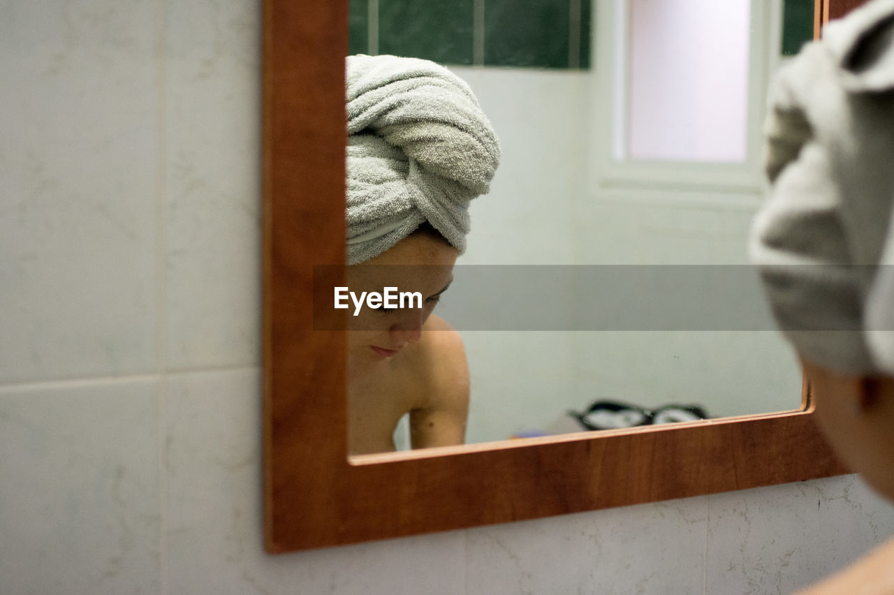 Reflection of woman with towel on mirror in bathroom
