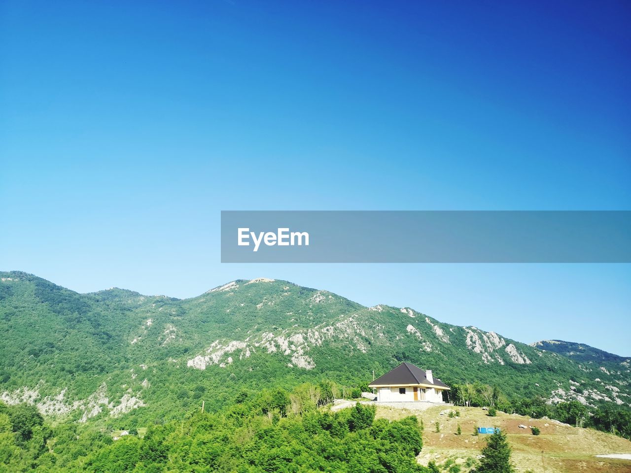 Scenic view of house and mountains against clear blue sky