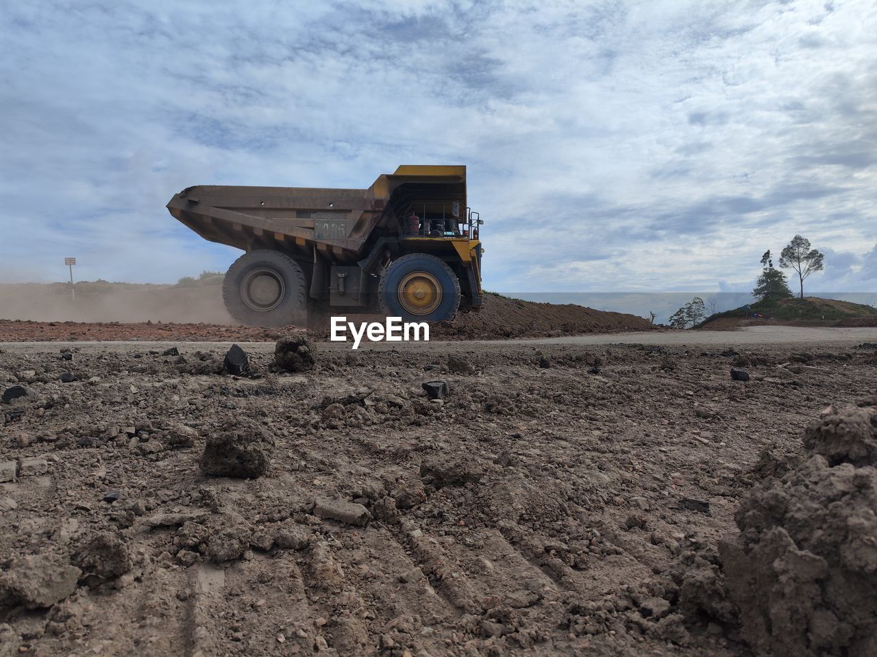 soil, transportation, sand, mode of transportation, field, sky, vehicle, industry, machinery, land, landscape, dirt, nature, land vehicle, construction industry, environment, construction machinery, off-roading, truck, cloud, day, natural environment, wheel, dump truck, no people, construction site, outdoors, motor vehicle, earth mover, digging, road, commercial land vehicle, rural scene, construction vehicle