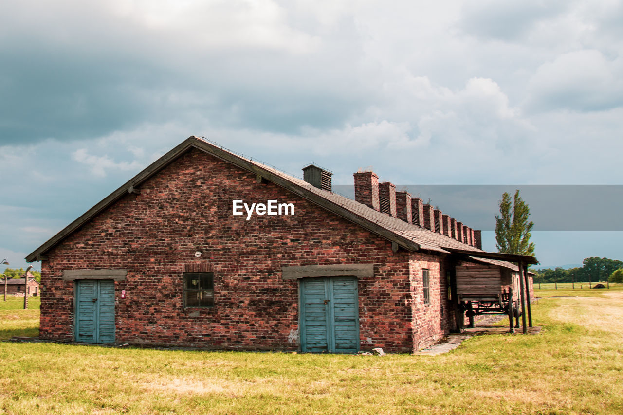 OLD HOUSE ON FIELD BY BUILDING AGAINST SKY