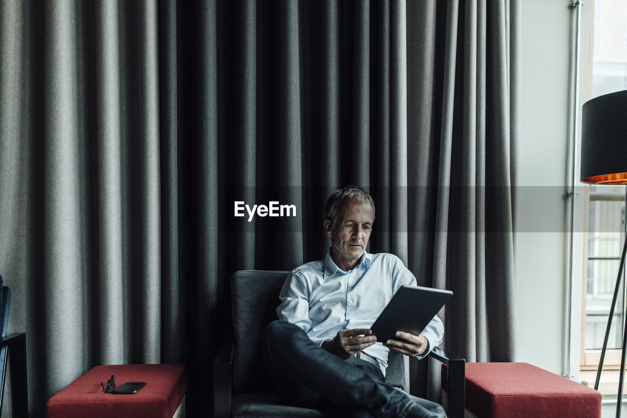 Serious businessman using digital tablet against gray curtain in office cafeteria