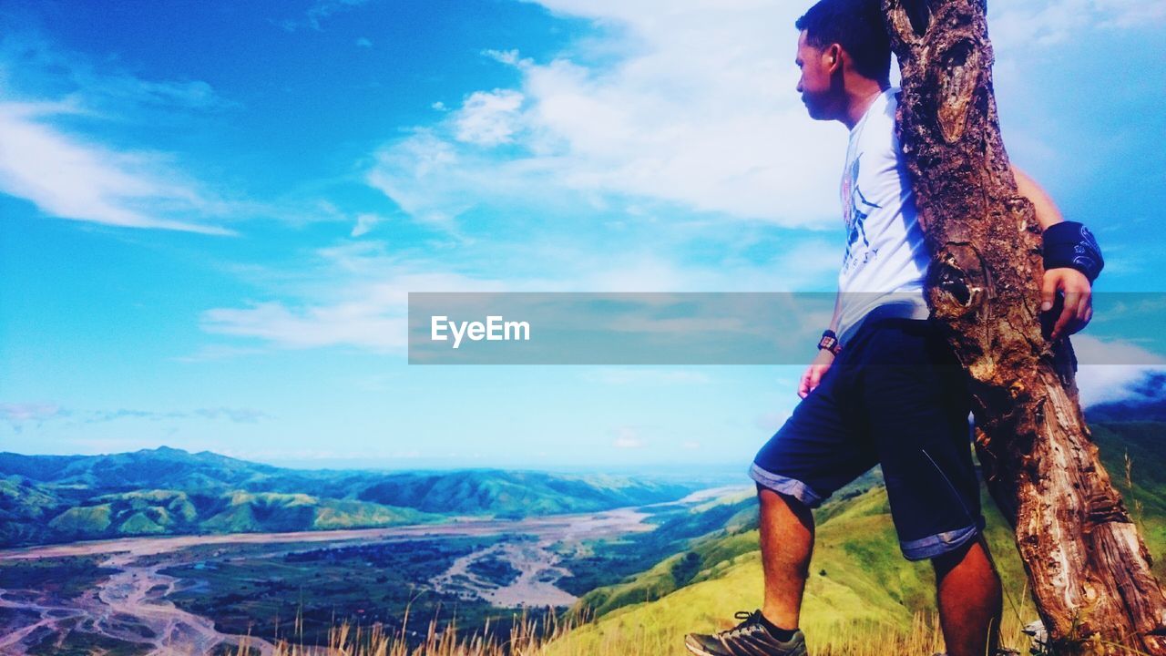 MAN STANDING ON LANDSCAPE AGAINST MOUNTAIN