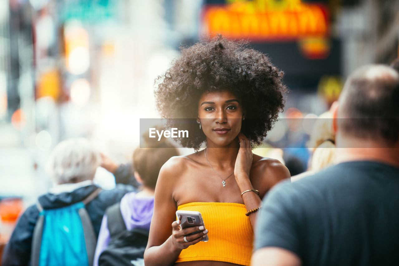 Portrait of confident young woman holding smart phone on city street