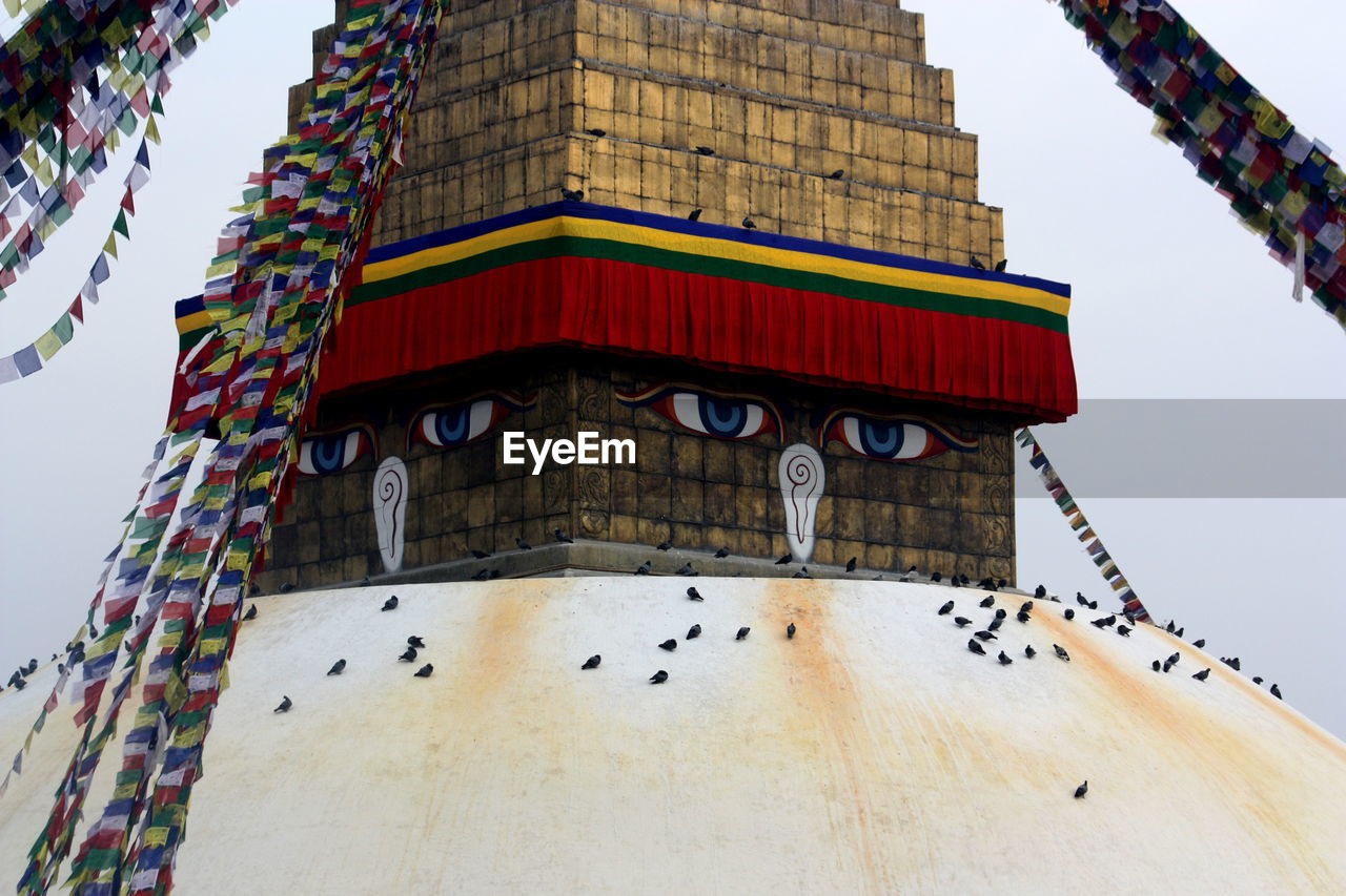 Low angle view of pigeons perching on bodnath stupa dome against sky