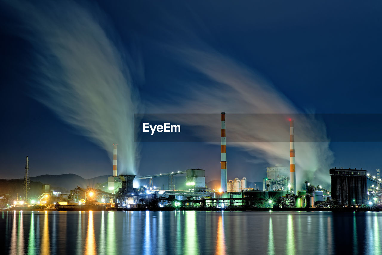 Panoramic view of illuminated factory against sky at night