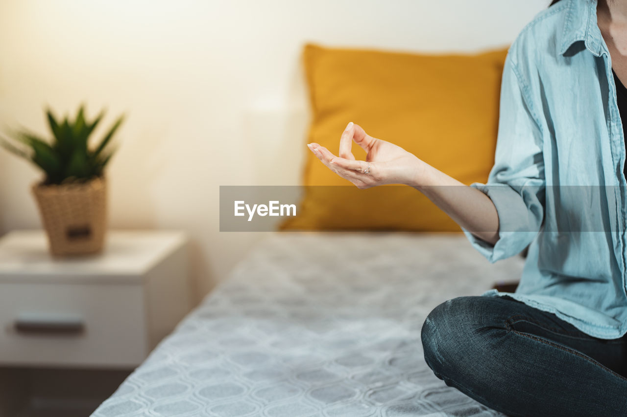 MIDSECTION OF WOMAN SITTING ON BED