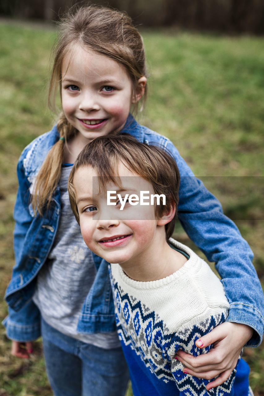 Portrait of smiling girl with brother standing on field