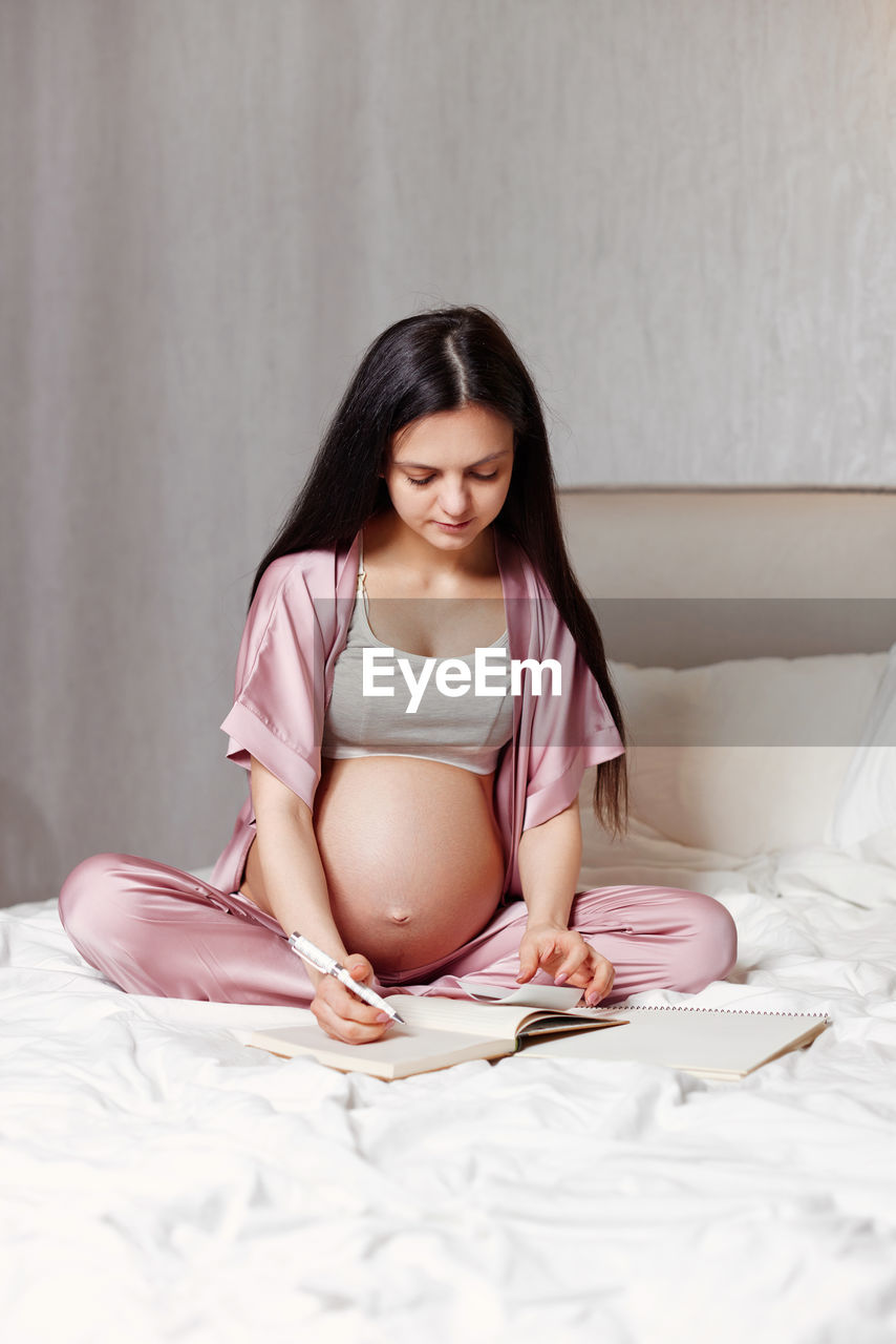 Pregnant woman writing on bed at home