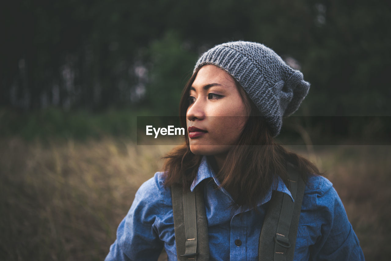 Close-up of thoughtful young woman wearing knit hat while standing on field