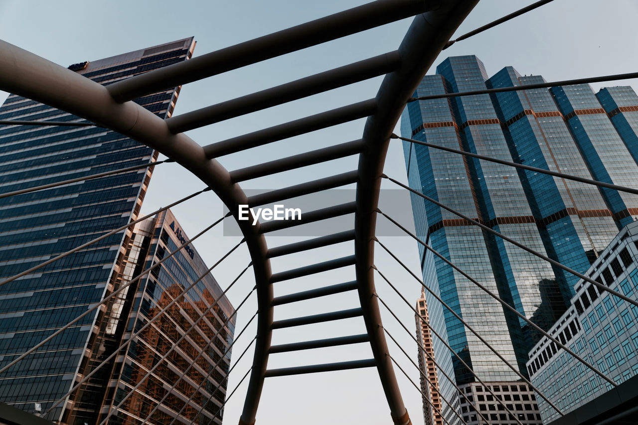 Low angle view of modern buildings against sky seen through bridge at sathon district