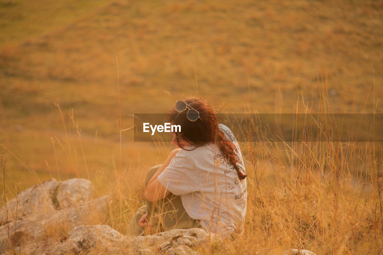 Side view of woman sitting on field during sunset