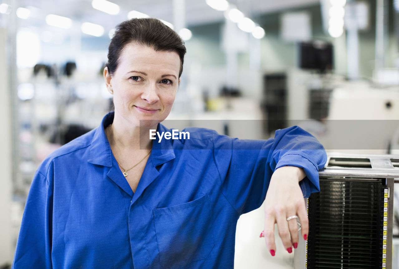 Front view portrait of confident female technician standing in industry