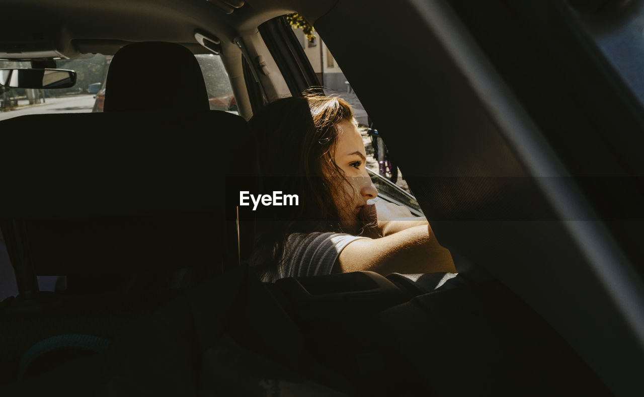 Pre-adolescent girl looking out of window while sitting in electric car during vacation