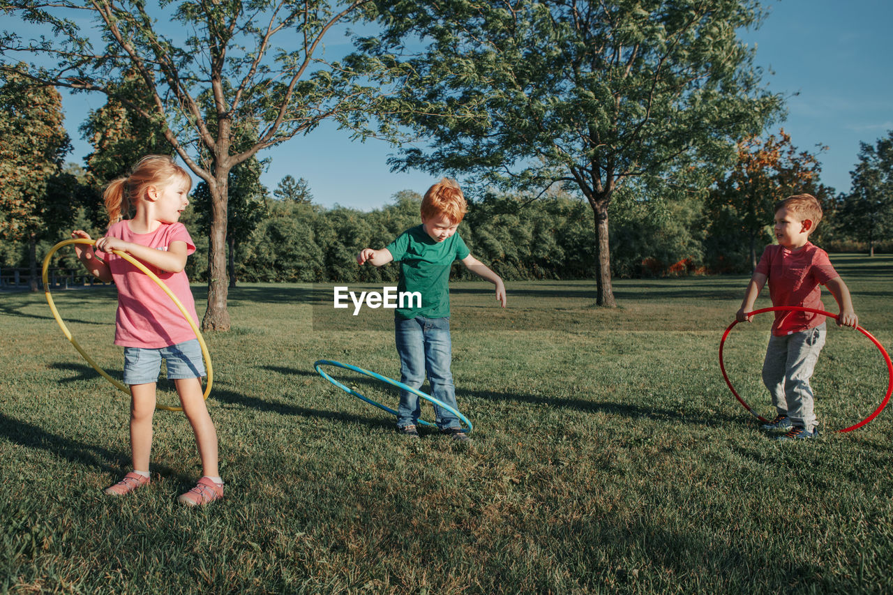 Full length of children playing with plastic hoops on grassy land in park