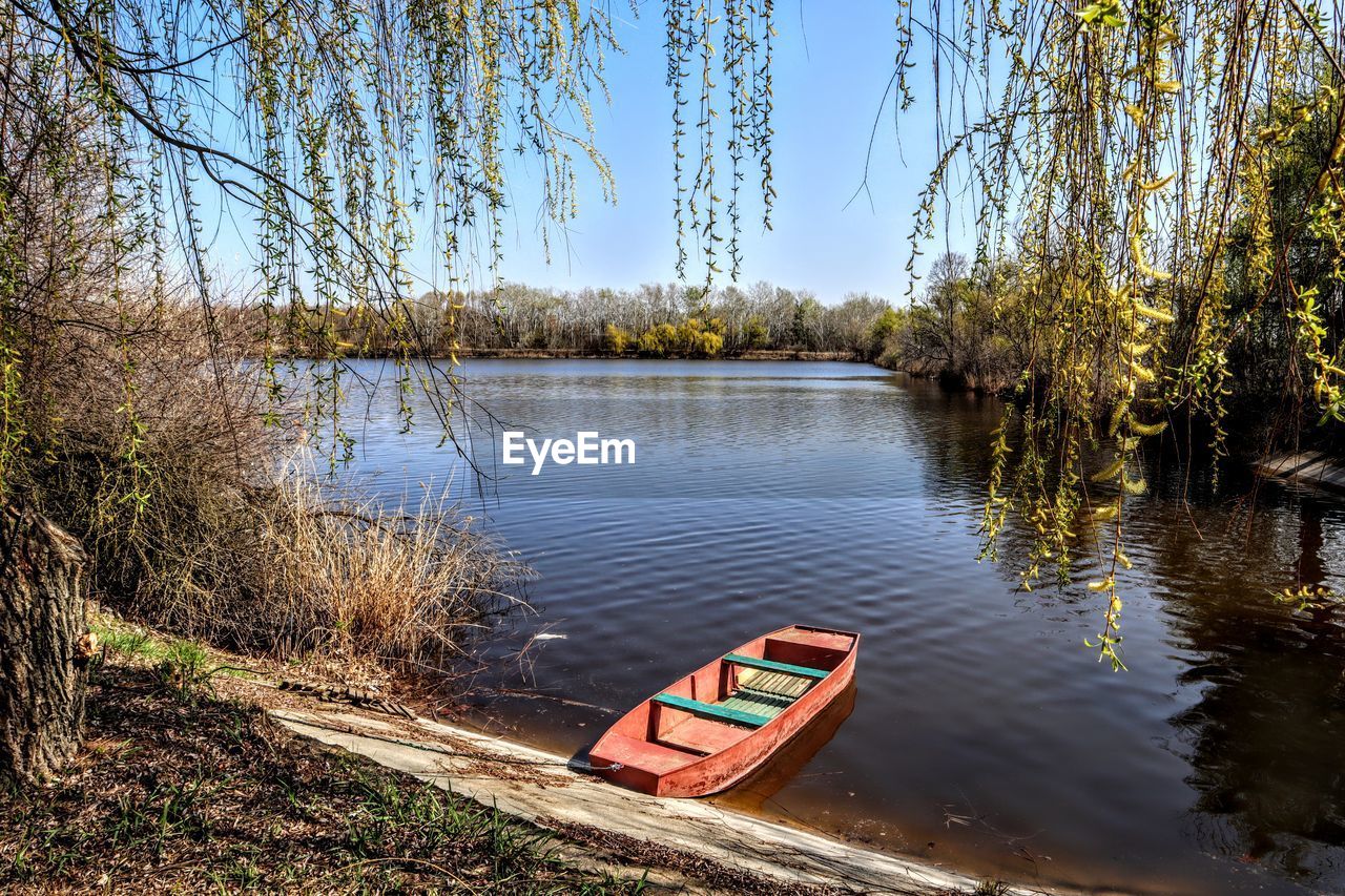 BOAT MOORED AT LAKESHORE AGAINST SKY