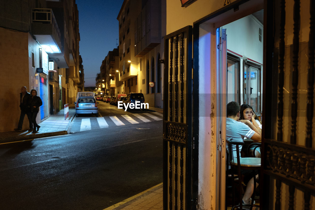 REAR VIEW OF WOMAN SITTING ON STREET AT NIGHT