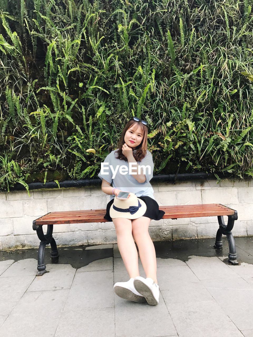 Portrait of young woman sitting on bench against plants