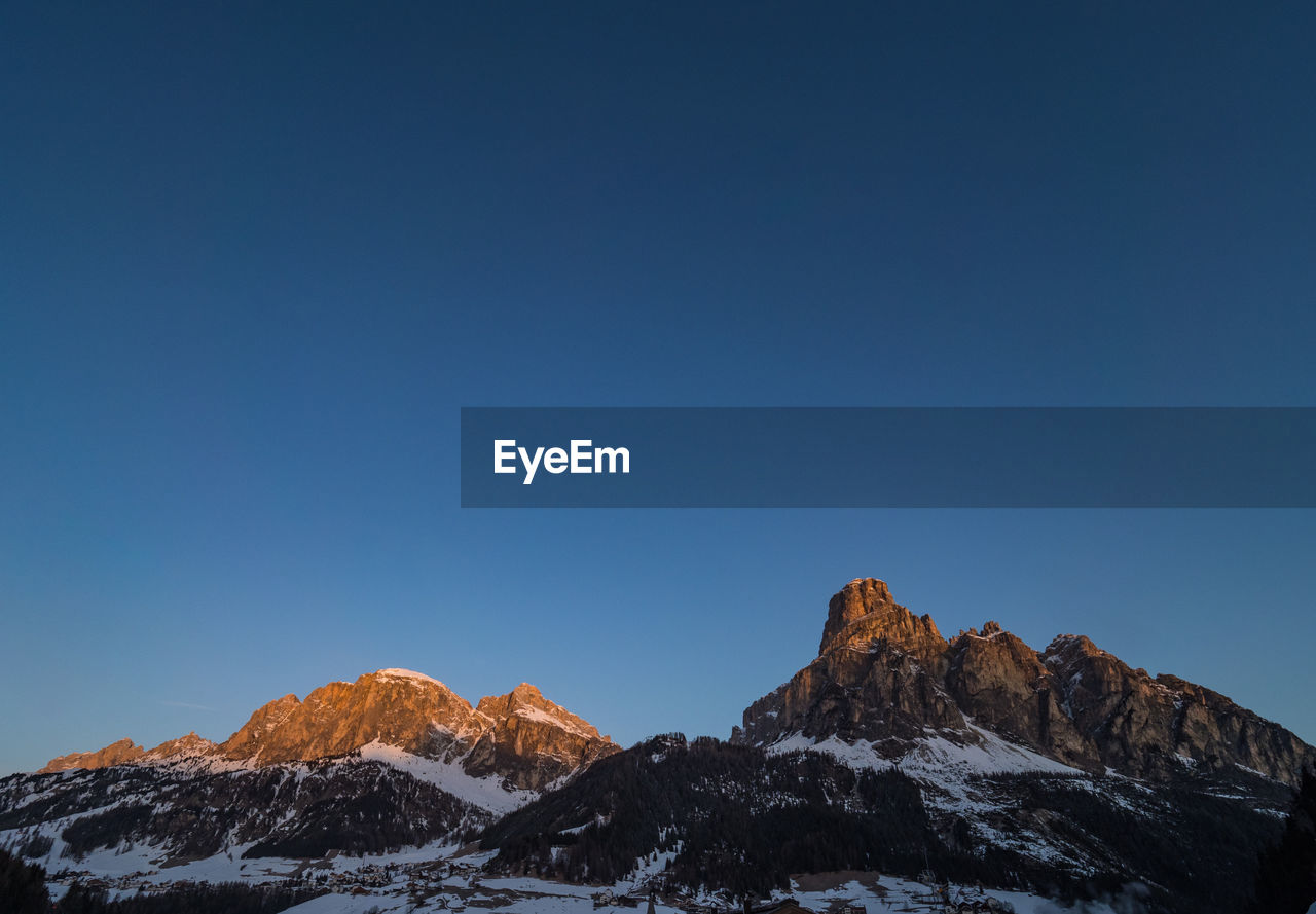 Scenic view of snowcapped mountains against clear blue sky at sunrise