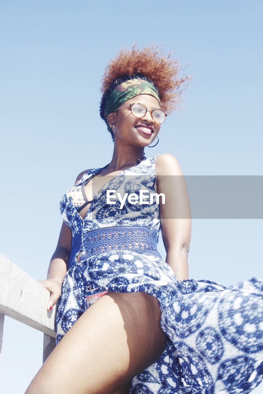 PORTRAIT OF SMILING YOUNG WOMAN AGAINST SKY