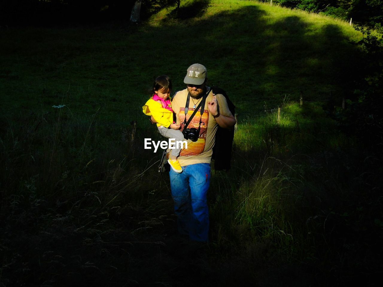 Man carrying daughter while walking through grassy field