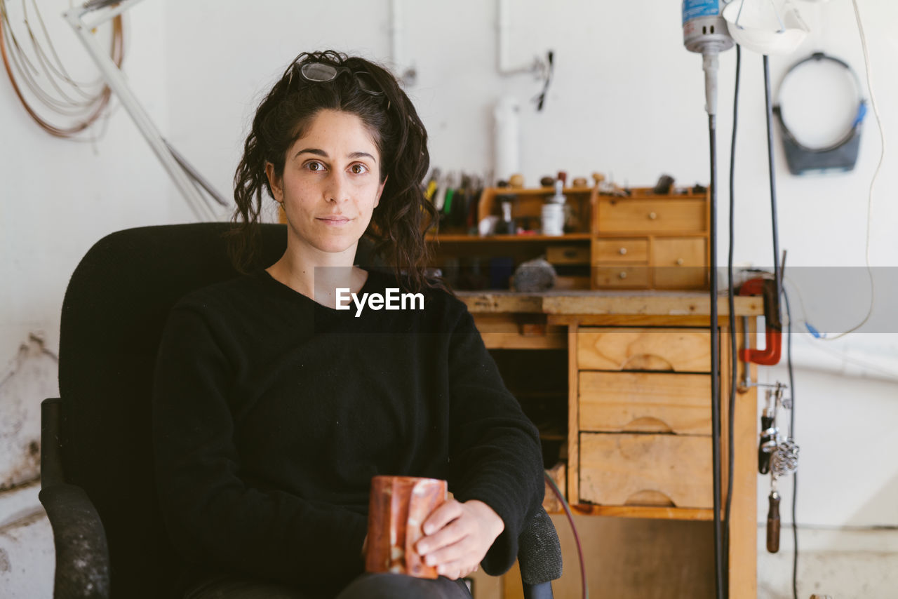 Casual photo of posterior women with mug at work desk in bright room