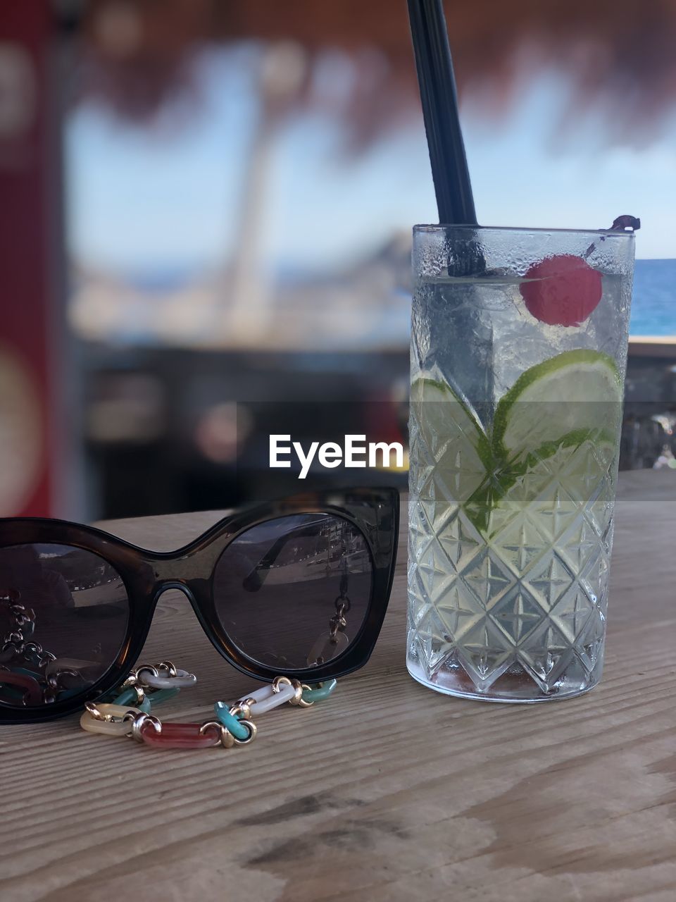 soft drink, drinking glass, food and drink, drink, straw, glass, drinking straw, refreshment, cocktail, glasses, household equipment, sunglasses, table, food, goggles, alcoholic beverage, summer, alcohol, fashion, cold temperature, focus on foreground, fruit, wood, no people, nature, day, close-up, outdoors, water, mojito, frozen, freshness, still life, beach