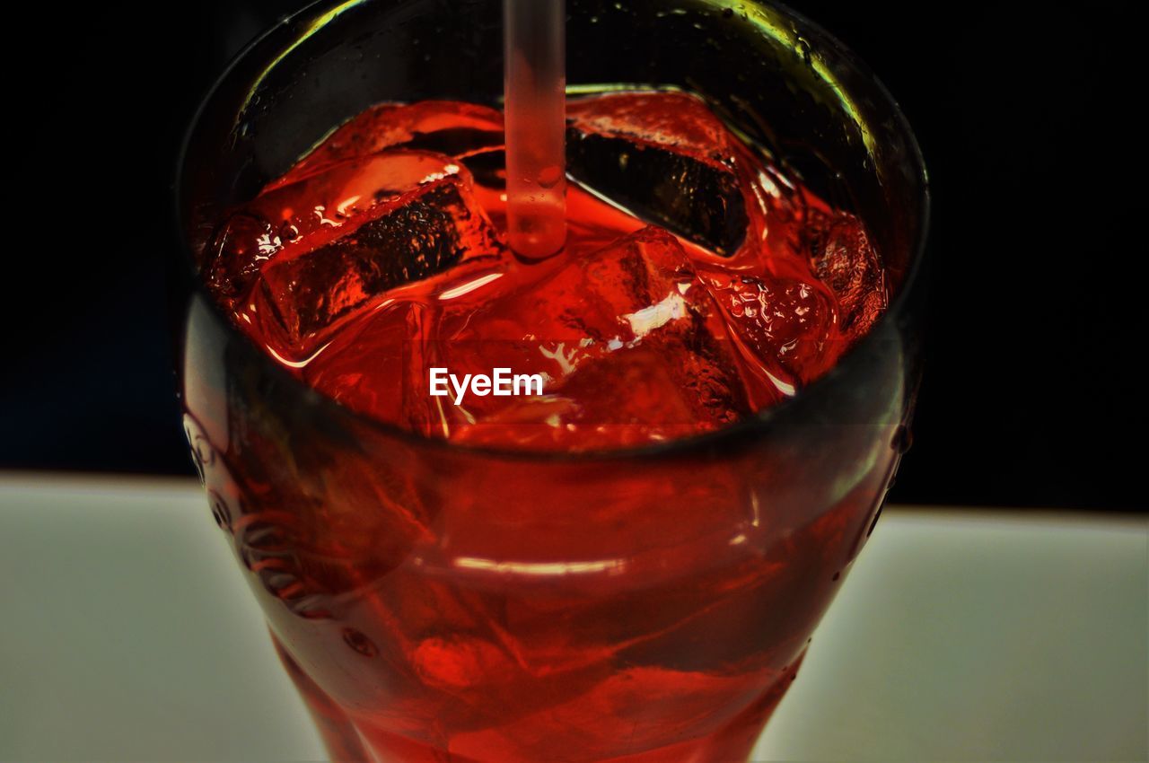 Close-up of fresh red drink with ice cubes and straw on table