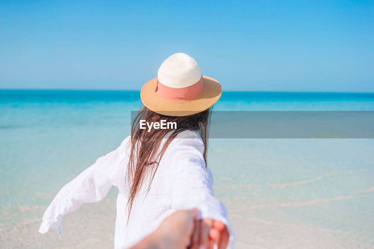 REAR VIEW OF WOMAN WEARING HAT ON BEACH