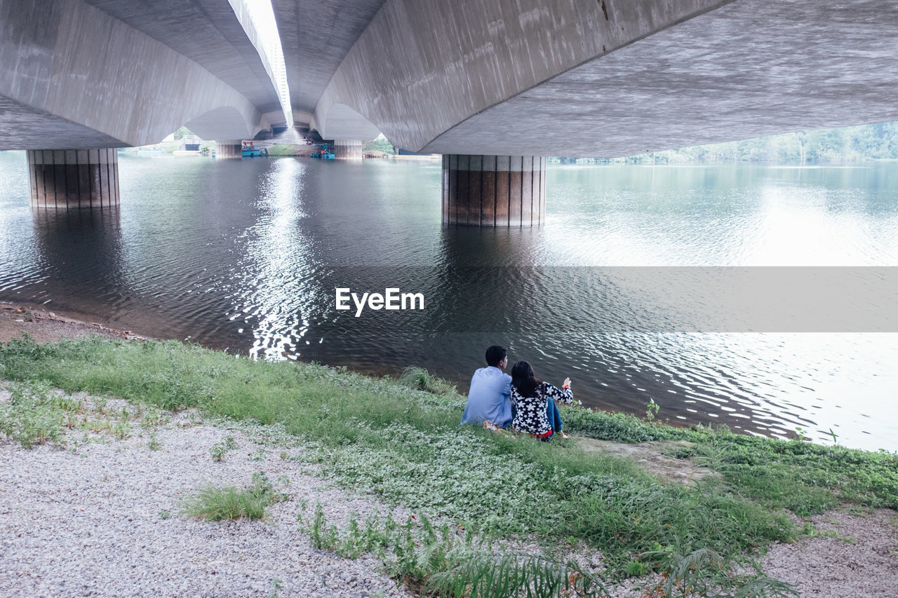 Couple sitting below bridge