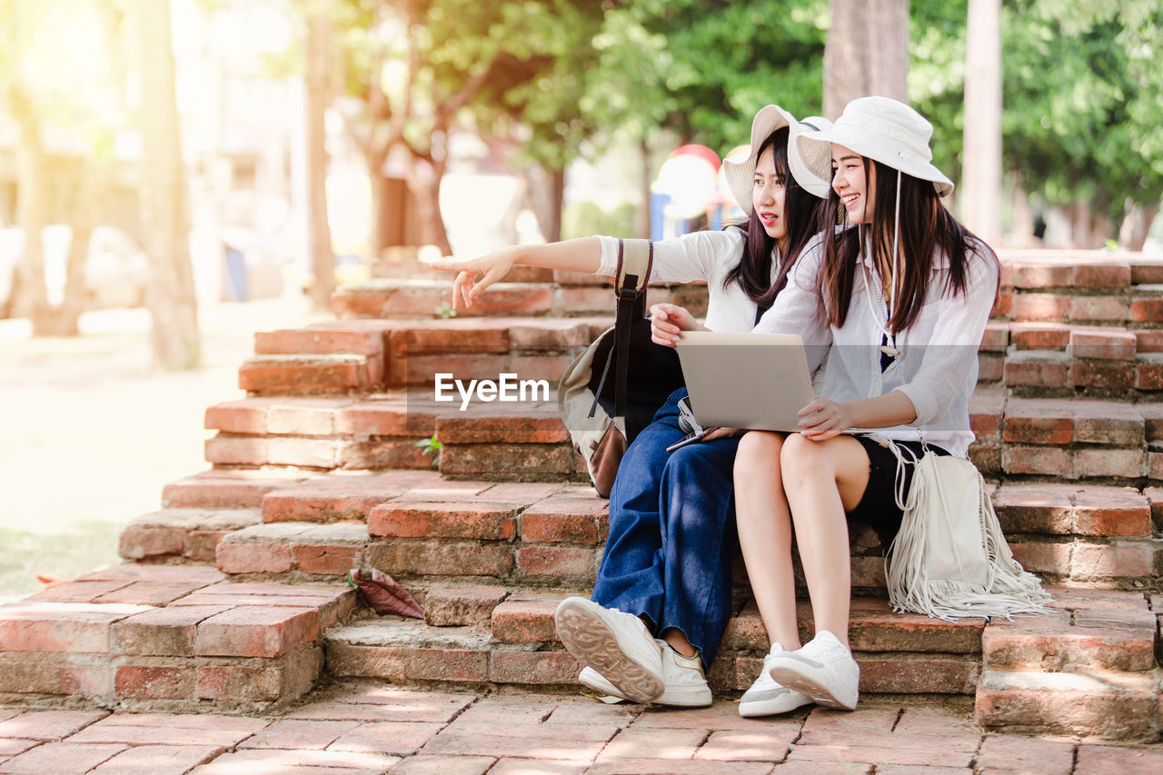 Woman pointing by friend using laptop while sitting on staircase