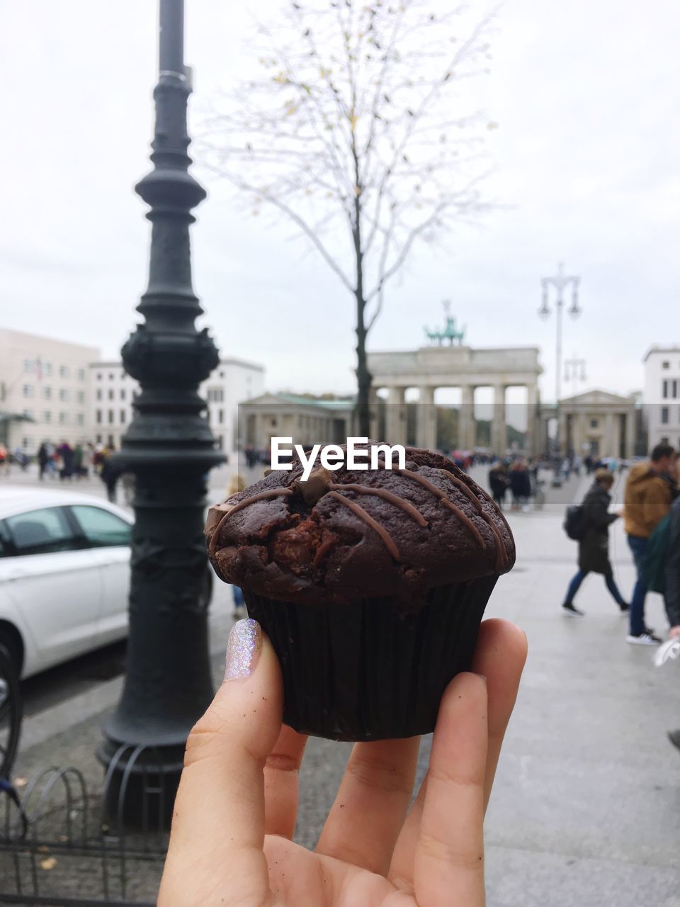 Close-up of human hand holding chocolate muffin in city