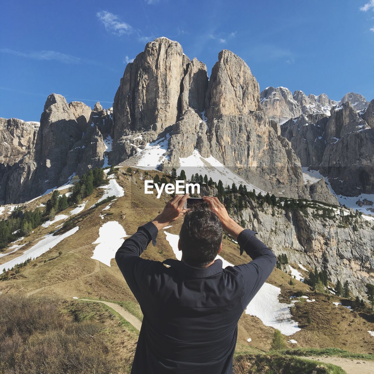 REAR VIEW OF MAN ON ROCKS AGAINST SKY