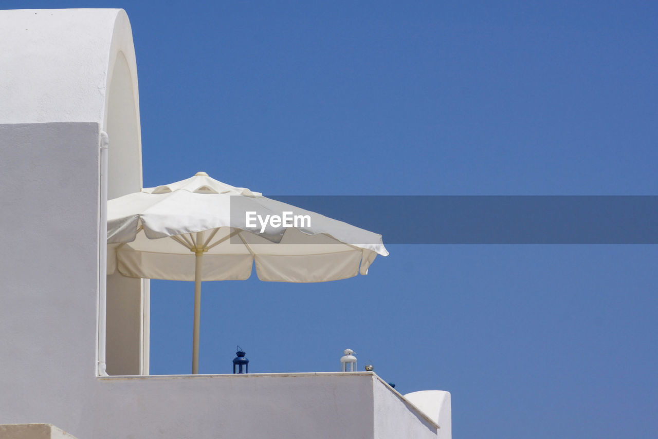 Low angle view of umbrella at balcony of building against clear blue sky