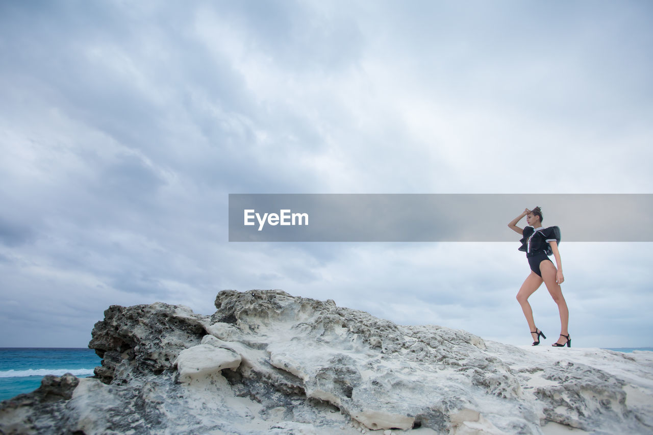 Woman posing on rock against sky