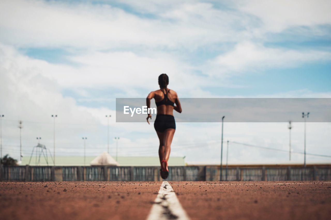 Rear view of female athlete running on track field against sky