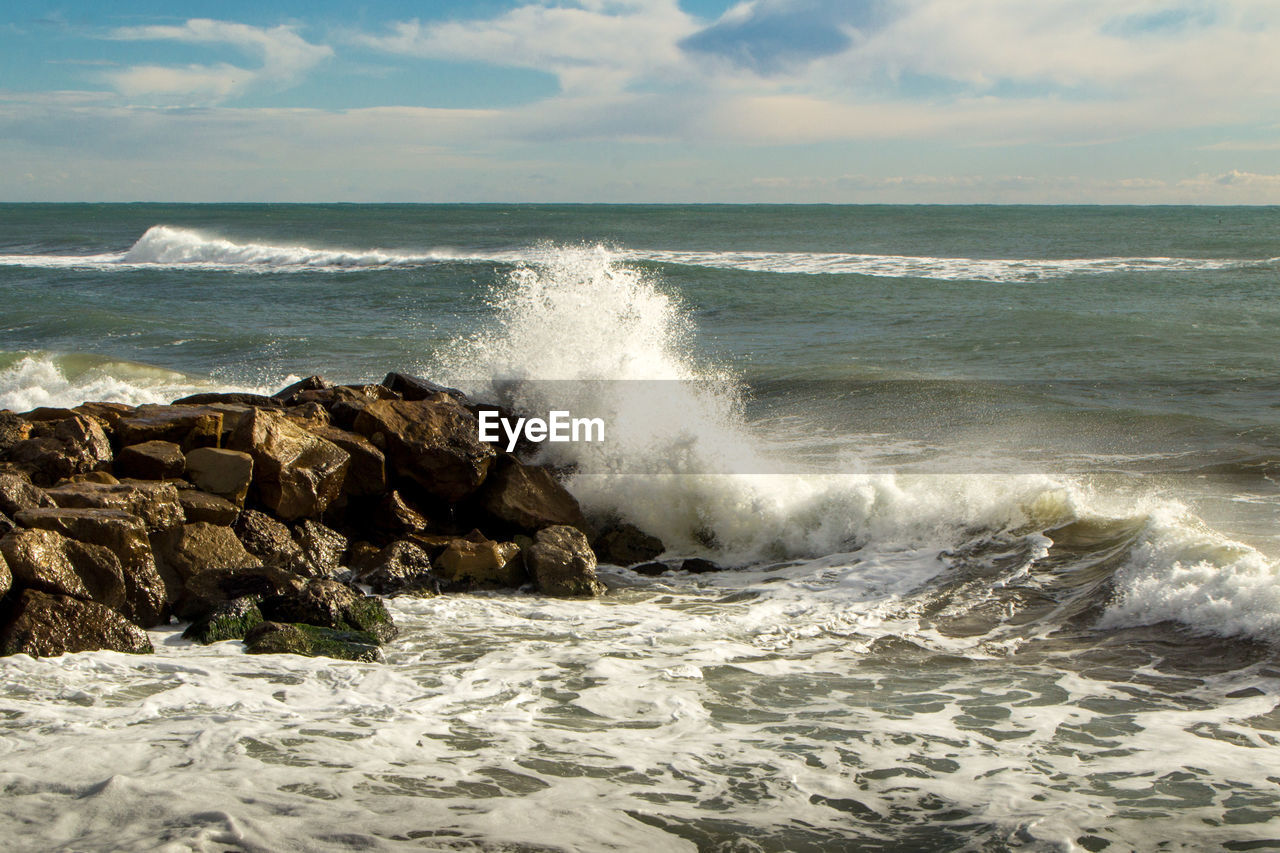 Scenic view of sea and waves splashing against the rocks in windy day