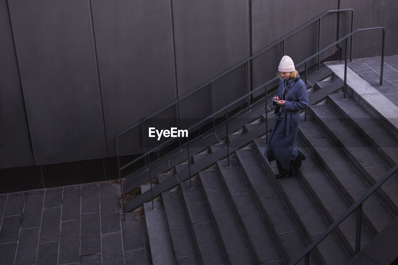 Young woman walking down stairs and using phone