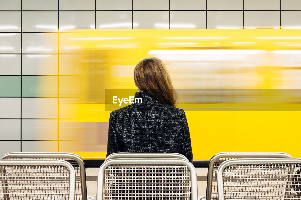 Rear view of woman sitting on bench at railroad station