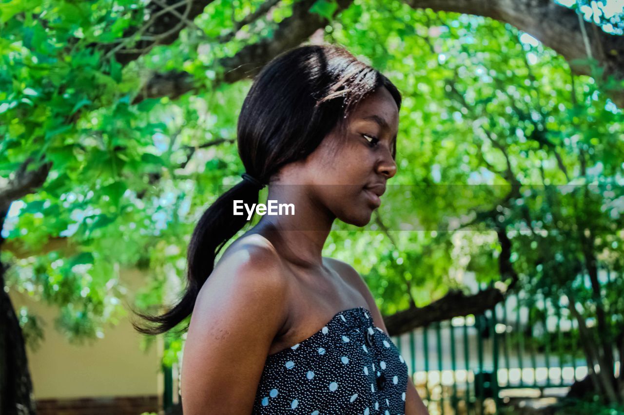 Young woman looking away while standing against trees